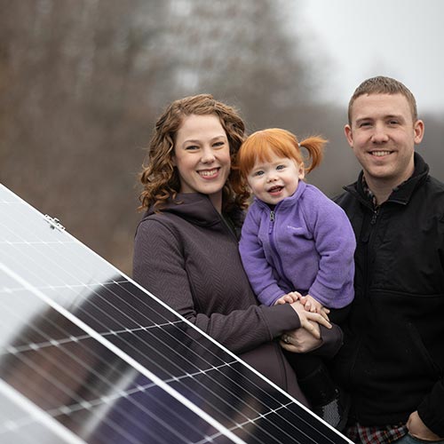Father, mother, and daughter standing next to a residential solar array