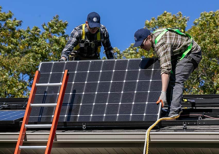 Two solar panel contractors installing a solar panel on a roof