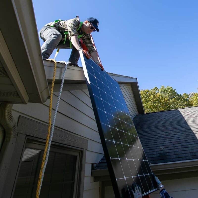 Contractors lifting a solar panel onto the roof of a home