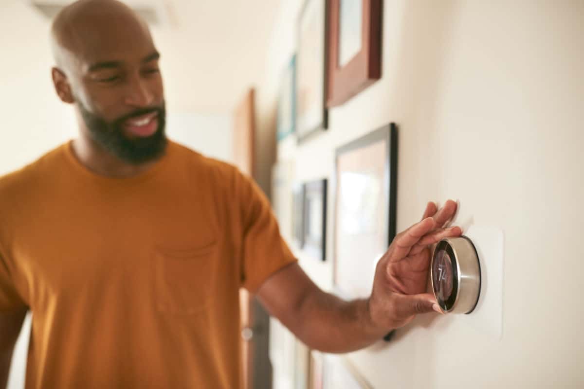 Man Adjusting Digital Central Heating Thermostat At Home